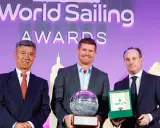 Tom Slingsby mit Auszeichnung bei den World Sailing Awards. Er hält eine Trophäe, daneben zwei Männer mit Geschenken.