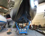 Schwarzer Bootsrumpf auf Stützen, bereit für den antifouling test. Glänzende Oberfläche reflektiert die Werkstatt.