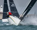 Segelboote kämpfen bei der Admirals Cup Regatta um die Wette. Gischt spritzt, die Crew sitzt tief.
