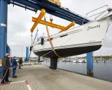 Segelboot "Sweety" wird für das unterwasserschiff reinigen aus dem Wasser gehoben. Männer sichern das Boot mit Seilen.