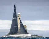 Segelboot mit schwarzen Segeln navigiert durch raue See am Fastnet Rock, ein dramatischer Moment im Fastnet Race.