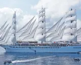 Ein majestätisches Segelschiff mit vollen weißen Segeln, das wie ein **sea cloud spirit** über das blaue Meer gleitet. Kleine Beiboote sind in der Nähe.