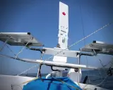 Weiße Windfahne mit kanadischer Flagge auf einem Segelboot, mit Solarpaneelen und dem blauen Himmel im Hintergrund.