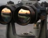 Fernglas-Werte: Ein Flugzeugträger und ein Hubschrauber spiegeln sich im Okular eines Fernglases bei Sonnenuntergang.