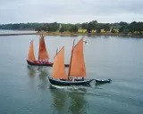 Drei traditionelle Segelboote mit orangefarbenen Segeln auf dem Wasser vor der Küste der Bretagne.