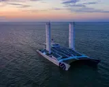 Der ENERGY OBSERVER, ein futuristisches Schiff mit Solarpaneelen und Windturbinen, gleitet bei Sonnenuntergang über das Meer.