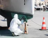 Person in Schutzanzug schleift den Rumpf eines Bootes. Die Arbeit am Boot schleifen erfordert Sorgfalt.