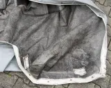 Graue, verschmutzte Persenning, bereit zum Reinigen. Die Innenseite zeigt deutliche Spuren von Schmutz und Verfärbungen.
