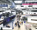 Besucher bestaunen Yachten auf einer Messe. Ein glänzendes, blaues Boot im Vordergrund erinnert an eine Fahrt auf dem kanal frankreich.