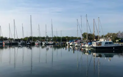 Segelboote und Motorboote liegen friedlich im Hafen Neuendorf, ihre Spiegelbilder tanzen auf dem ruhigen Wasser.