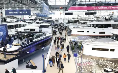 Besucher bestaunen Yachten auf einer Messe. Ein glänzendes, blaues Boot im Vordergrund erinnert an eine Fahrt auf dem kanal frankreich.