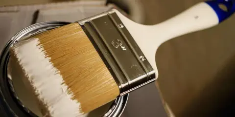 Pinsel mit weißer Farbe, bereit, ein Holzboot zu lackieren.