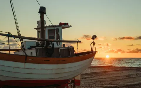 Ein Fischerboot liegt am Strand, während die Sonne im Meer versinkt. Der Unterschied zwischen einem Schiff und einem Boot wird hier deutlich: Dieses kleine Boot ist bereit für die nächste Fahrt.