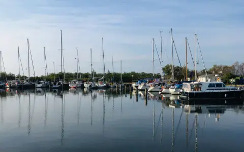Segelboote und Motorboote liegen friedlich im Hafen Neuendorf, ihre Spiegelbilder tanzen auf dem ruhigen Wasser.