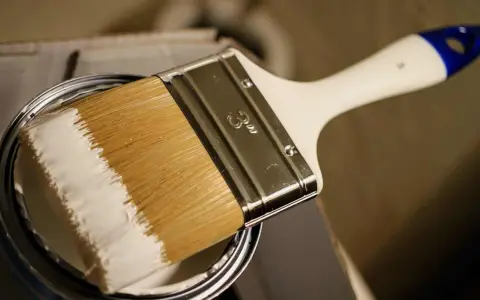 Pinsel mit weißer Farbe, bereit, ein Holzboot zu lackieren.