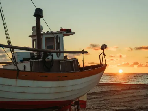Ein Fischerboot liegt am Strand, während die Sonne im Meer versinkt. Der Unterschied zwischen einem Schiff und einem Boot wird hier deutlich: Dieses kleine Boot ist bereit für die nächste Fahrt.