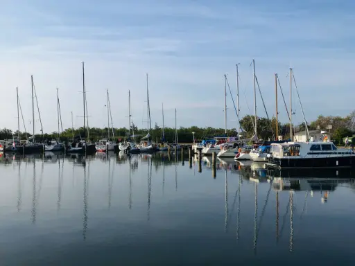Segelboote und Motorboote liegen friedlich im Hafen Neuendorf, ihre Spiegelbilder tanzen auf dem ruhigen Wasser.