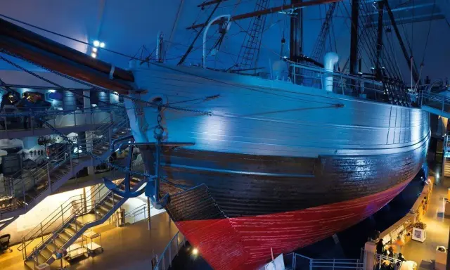 Ein historisches **fram schiff** mit Anker, umgeben von Treppen und Ausstellungsbereichen, in blauem Licht.