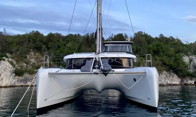 Ein moderner Katamaran mit zwei Rümpfen, der wie ein schwimmendes Haus aussieht, ankert vor einer bewaldeten Küste.
