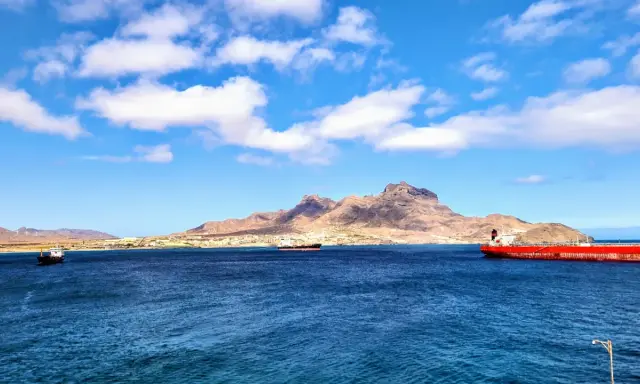 Blick auf die Bucht von Mindelo, Kap Verde, mit Schiffen im tiefblauen Wasser und einer bergigen Küstenlinie im Hintergrund.
