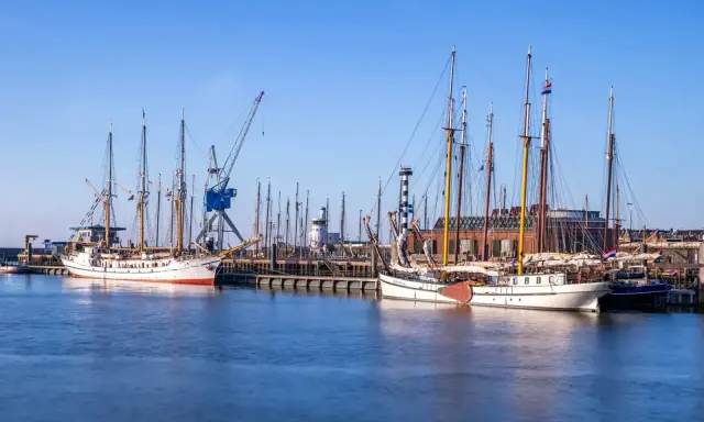 Segelschiffe im Harlingen Hafen, ein Kran ragt in den blauen Himmel.