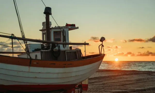 Ein Fischerboot liegt am Strand, während die Sonne im Meer versinkt. Der Unterschied zwischen einem Schiff und einem Boot wird hier deutlich: Dieses kleine Boot ist bereit für die nächste Fahrt.