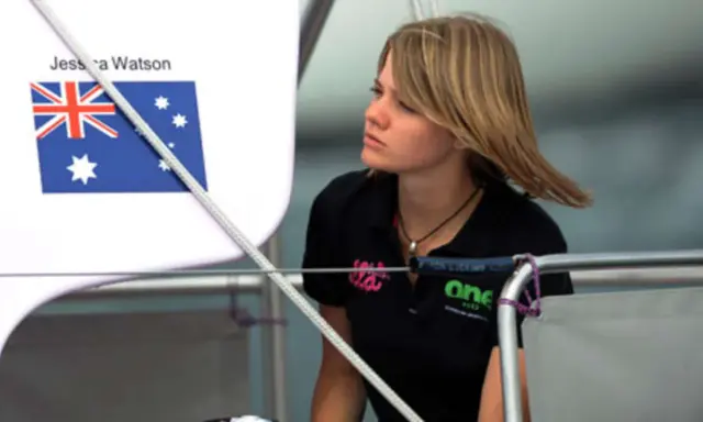 Jessica Watson heute, blickt nachdenklich auf dem Boot. Die australische Flagge ist im Hintergrund zu sehen.