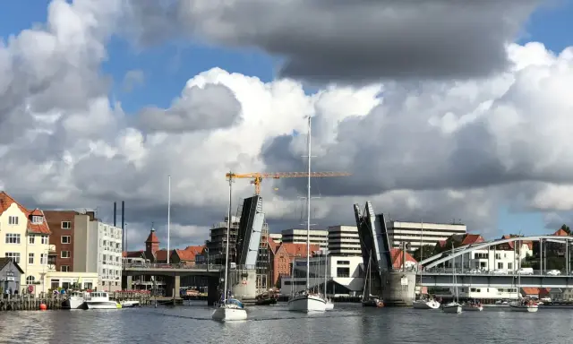 Sonderborg Hafen mit geöffneter Klappbrücke, Segelbooten und Gebäuden unter dramatischem Wolkenhimmel.