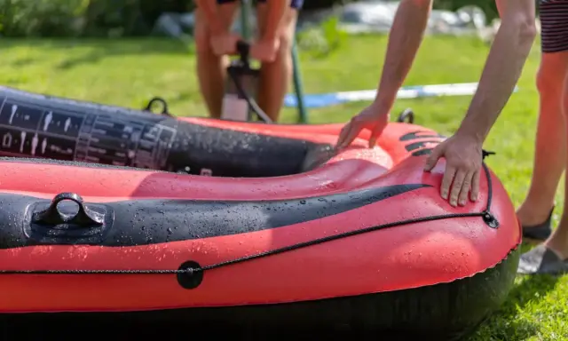 Hände bereiten das Schlauchboot vor, während im Hintergrund jemand pumpt.