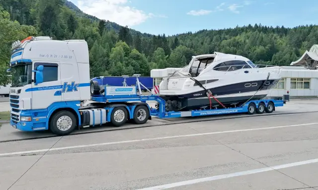 Ein LKW transportiert eine weiße Yacht auf einem Tieflader. Informieren Sie sich über bootstransport kosten für Ihre nächste Überführung.