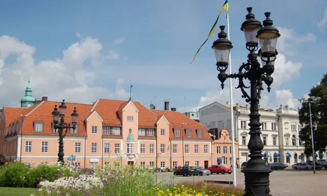 Blumen blühen am Karlskrona Hafen. Ein prächtiges Gebäude mit orangem Dach und eine schwedische Flagge im Wind.