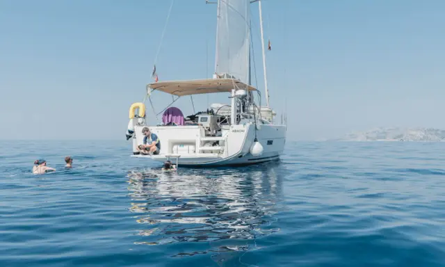 Erfahrungen, wenn du der Crew beitrittst: Ein Mann sitzt auf einer Yacht, während andere im Meer schwimmen.