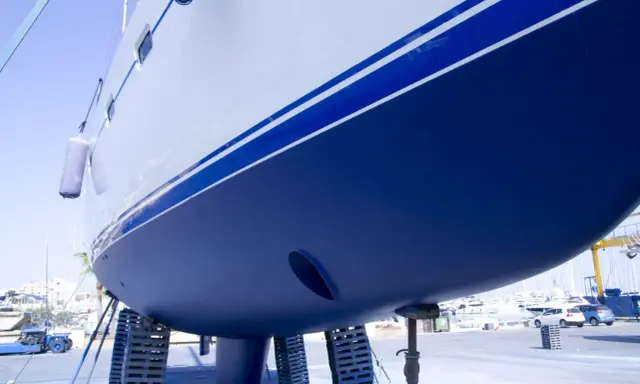 Der blaue **segelboot rumpf** mit weißen Streifen ruht auf Stützen im Hafen.