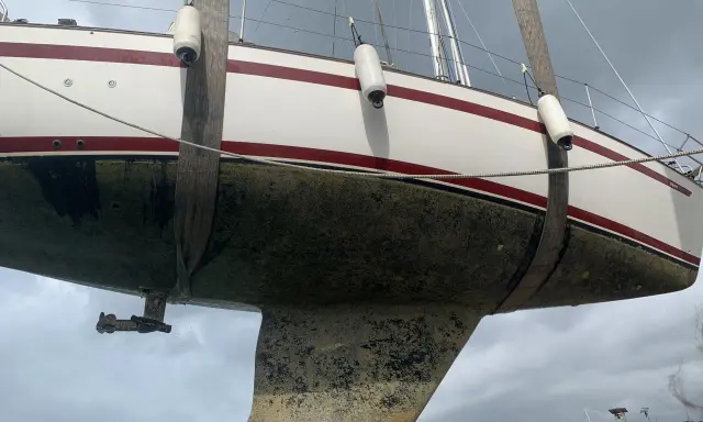 Segelboot wird angehoben, der Rumpf ist mit Algen bedeckt und bereit für die Behandlung mit Epoxidharz zum Streichen.