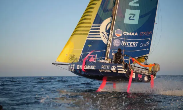 Segelboot mit pinken Foils rast über die Wellen. Ein Skipper steuert das Boot bei der Mini Transat Regatta.