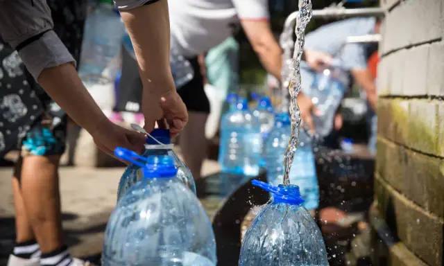 Menschen füllen Wasser in große Plastikflaschen. Die Frage, wie lange bleibt Wasser im Kanister frisch, ist hier relevant.