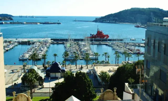 Der Cartagena Hafen mit vielen Segelbooten und einem roten Rettungsboot. Palmen säumen die Promenade.