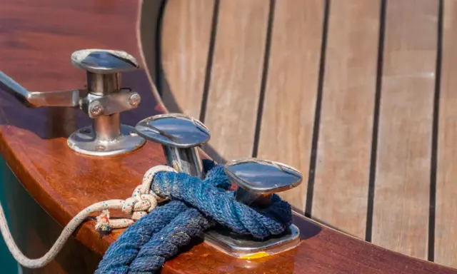 Detailaufnahme eines frisch verlegten Teakdecks mit polierten Klampen und Seilen.