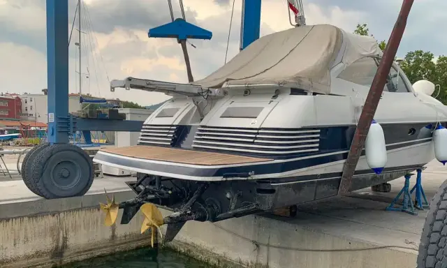 Ein luxuriöses Motorboot wird für das Winterlager aus dem Wasser gehoben. Zwei goldene Propeller ragen aus dem Rumpf.