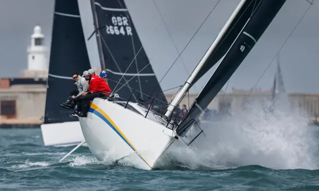 Segelboote kämpfen bei der Admirals Cup Regatta um die Wette. Gischt spritzt, die Crew sitzt tief.