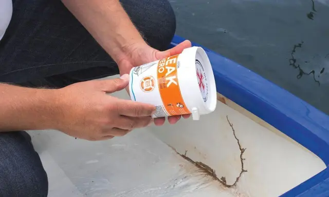 Person hält Dose mit Dichtmittel, um ein Boot abzudichten. Riss im Bootsrumpf sichtbar.