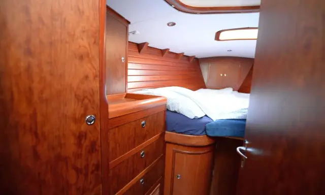 Gemütliches Bett mit gestreifter Bettwäsche im Innenbereich einer Segelyacht. Holzverkleidung und Schränke schaffen eine warme Atmosphäre.