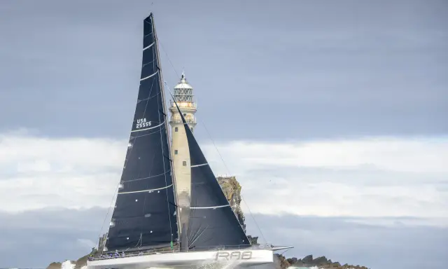 Segelboot mit schwarzen Segeln navigiert durch raue See am Fastnet Rock, ein dramatischer Moment im Fastnet Race.