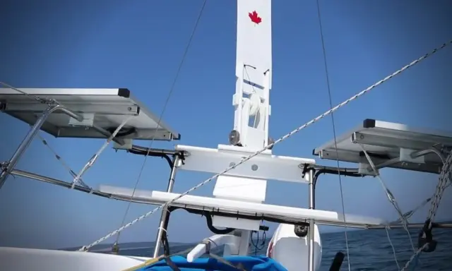 Weiße Windfahne mit kanadischer Flagge auf einem Segelboot, mit Solarpaneelen und dem blauen Himmel im Hintergrund.