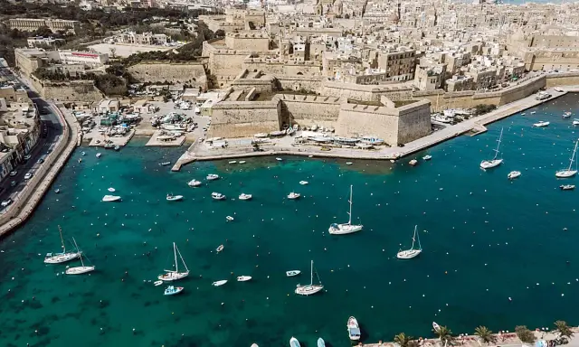 Segeln in Malta: Boote und Yachten im türkisfarbenen Wasser vor einer historischen Stadtkulisse mit Festungsmauern.