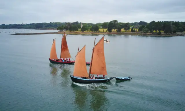 Drei traditionelle Segelboote mit orangefarbenen Segeln auf dem Wasser vor der Küste der Bretagne.