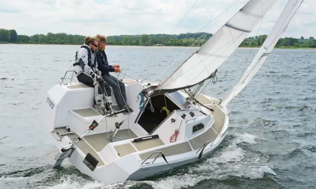 Zwei Segler genießen eine Fahrt auf einer Sailart 20. Das Boot gleitet durch das Wasser, die Segel sind gesetzt.