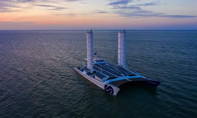 Der ENERGY OBSERVER, ein futuristisches Schiff mit Solarpaneelen und Windturbinen, gleitet bei Sonnenuntergang über das Meer.