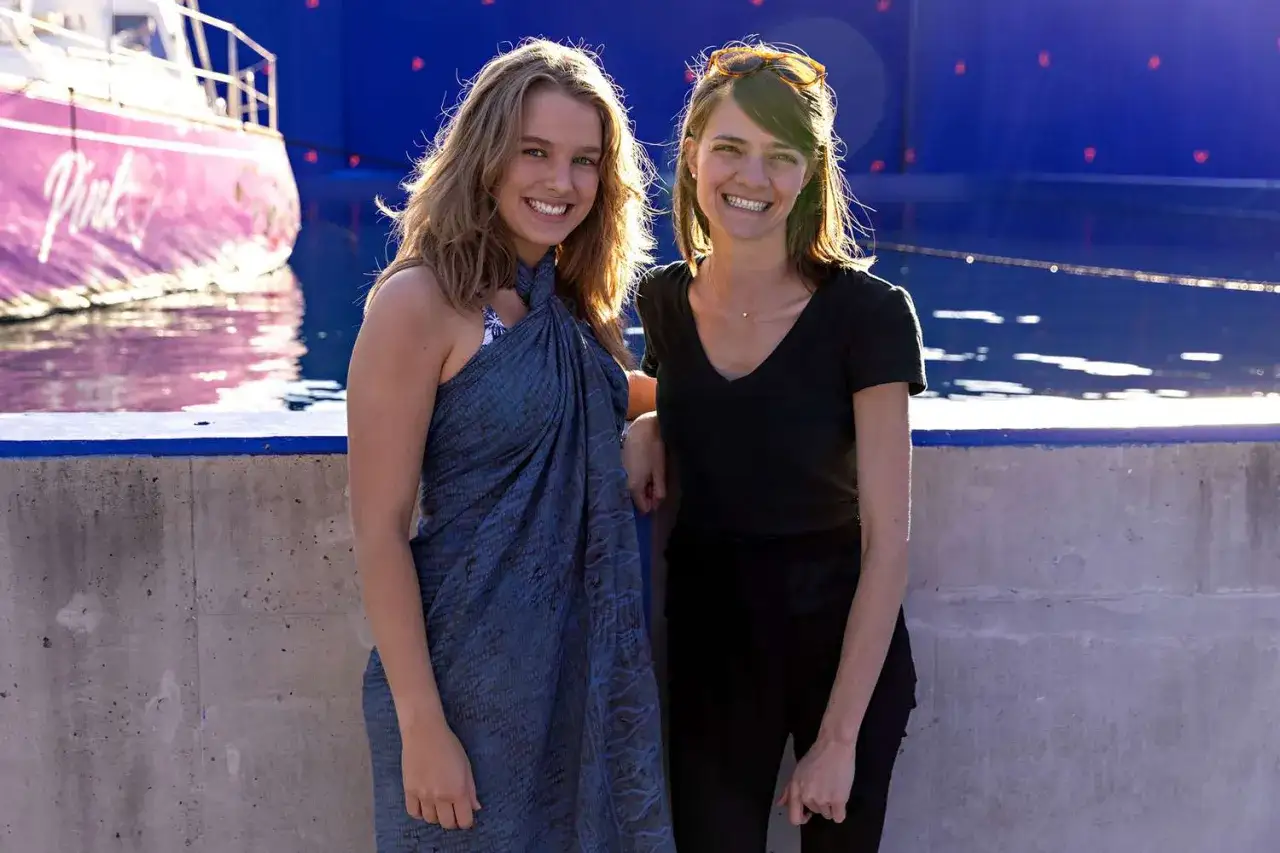 Jessica Watson heute, lächelnd neben einer Freundin, mit dem pinken Boot