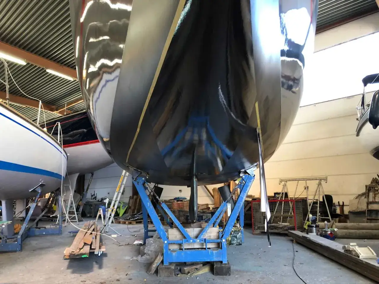 Schwarzer Bootsrumpf auf Stützen, bereit für den antifouling test. Glänzende Oberfläche reflektiert die Werkstatthalle.